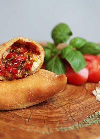 Calzone with red peppers and cheese, garnished with basil and tomatoes on a wooden board.