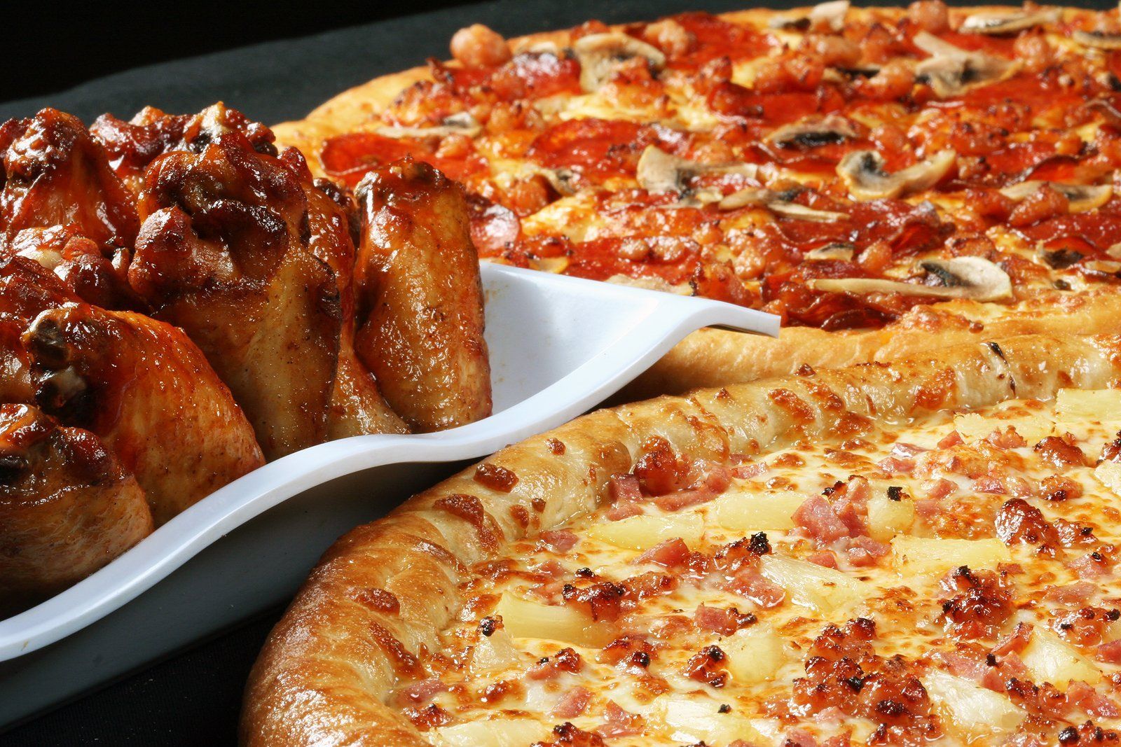 Pizza and wings: pepperoni pizza, ham and pineapple pizza, and baked chicken wings on a white serving plate.