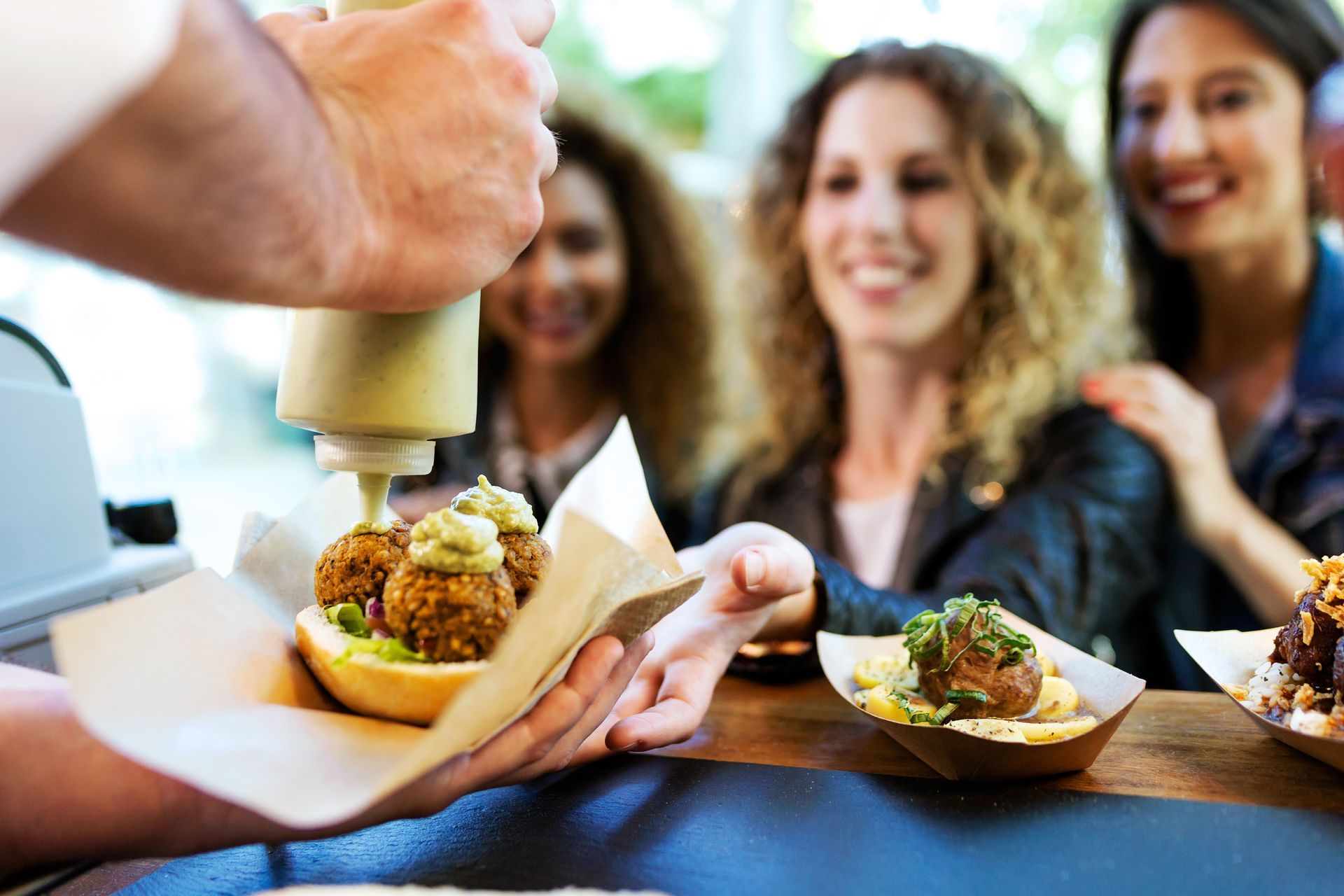 A group of women are sitting at a table eating food from a food truck.