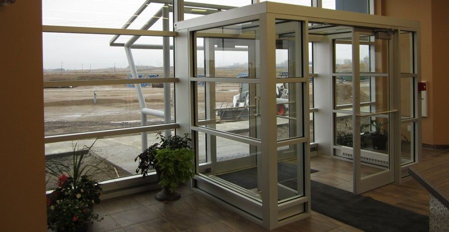 Porte-fenêtre coulissante noire sur la terrasse, avec des plantes et des arbres verts en arrière-plan.