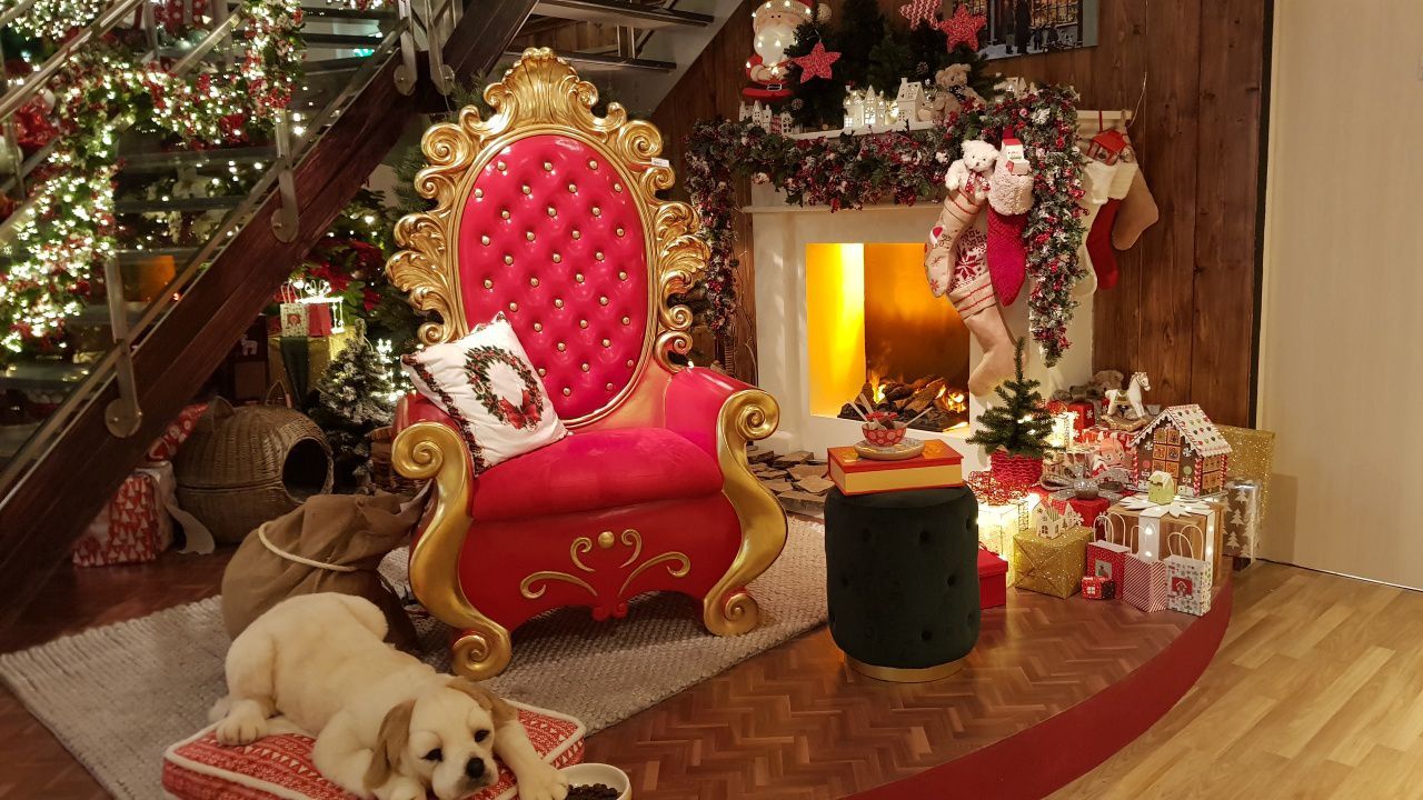 A dog is sitting in a santa claus chair in front of a fireplace.