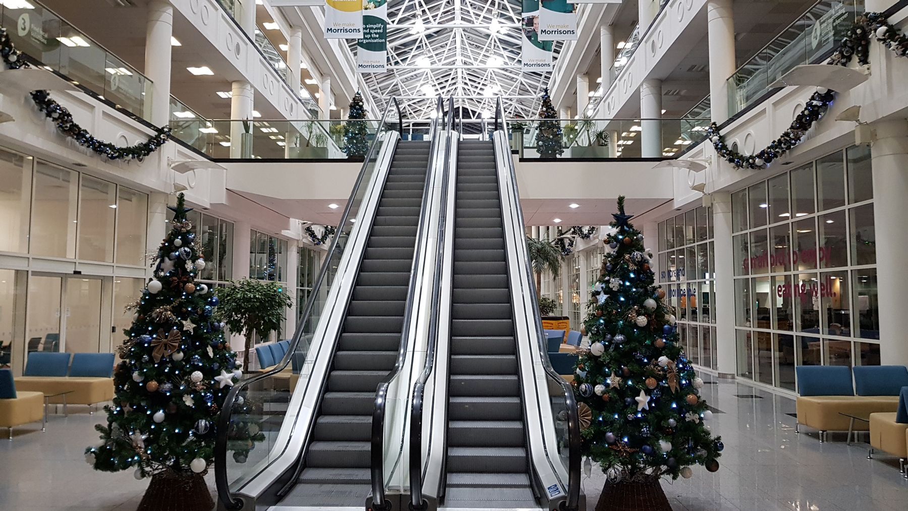 A shopping mall with christmas trees and an escalator decorated for christmas.