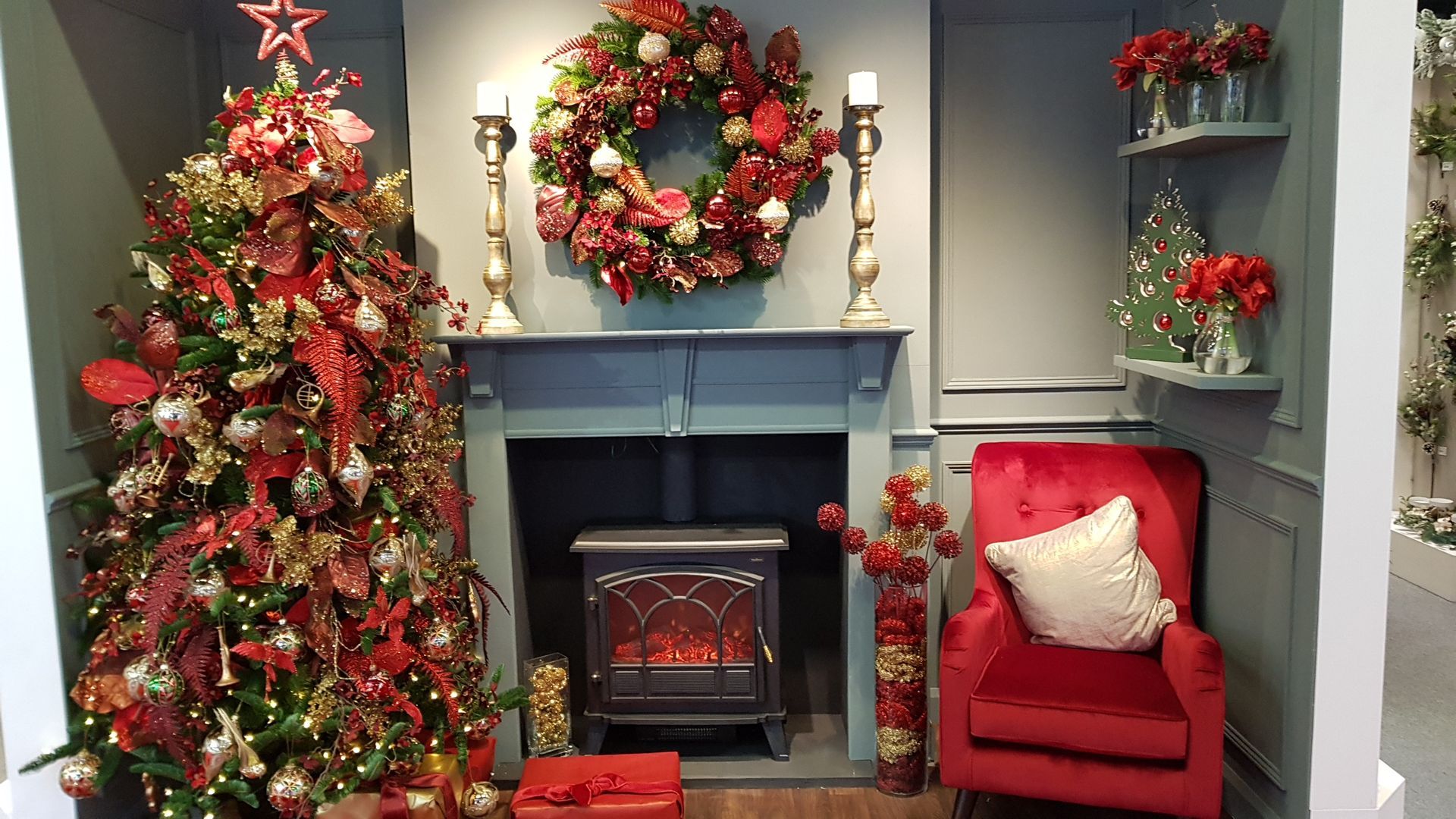 A living room decorated for christmas with a fireplace , chair , christmas tree and wreath.