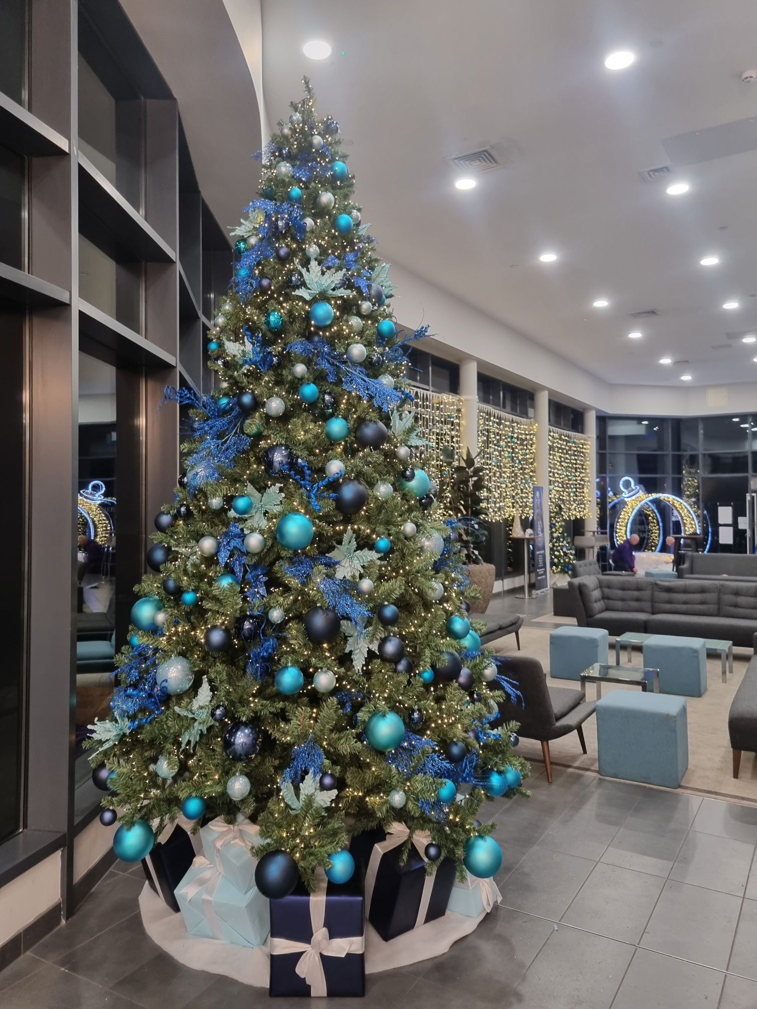 A large christmas tree decorated in blue and silver is in a lobby.