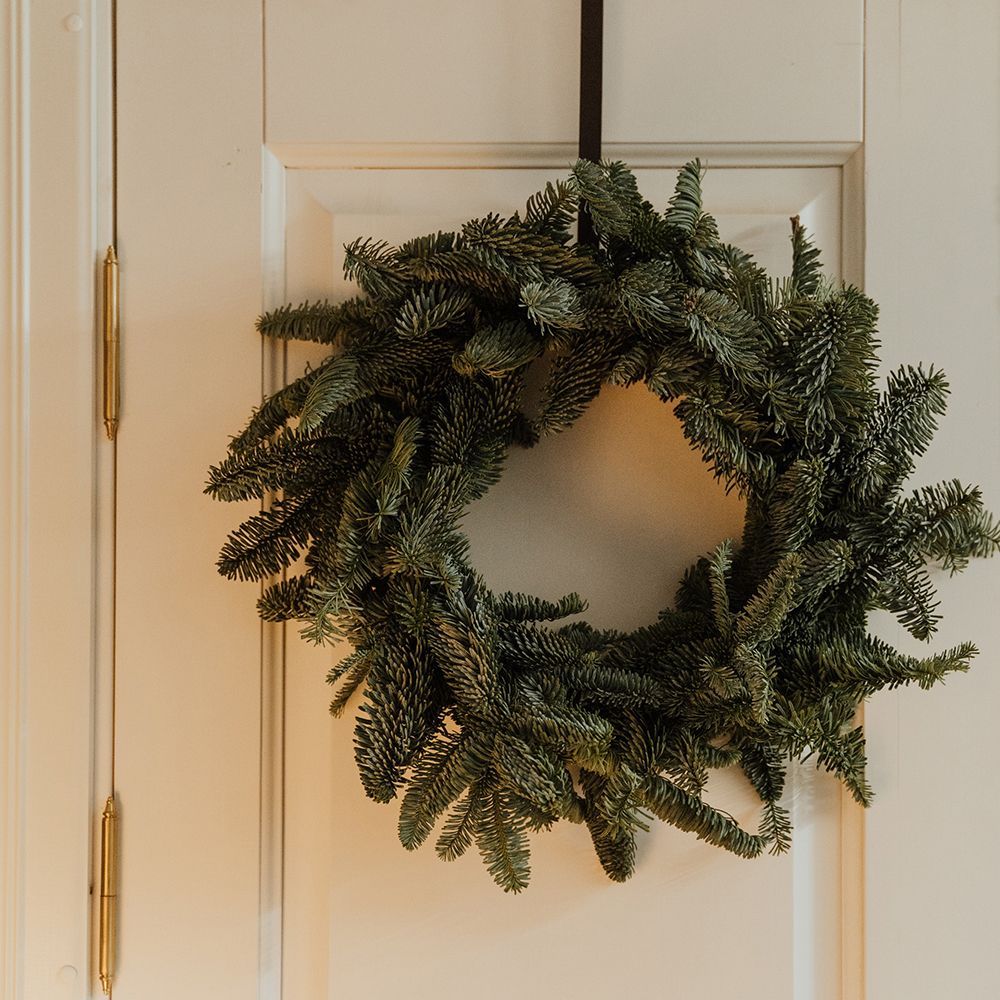 A christmas wreath is hanging on a white door.