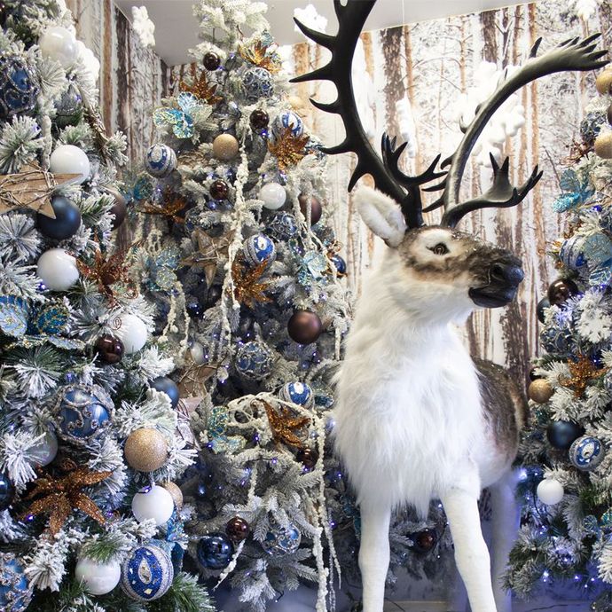 A stuffed reindeer is standing in front of a christmas tree.