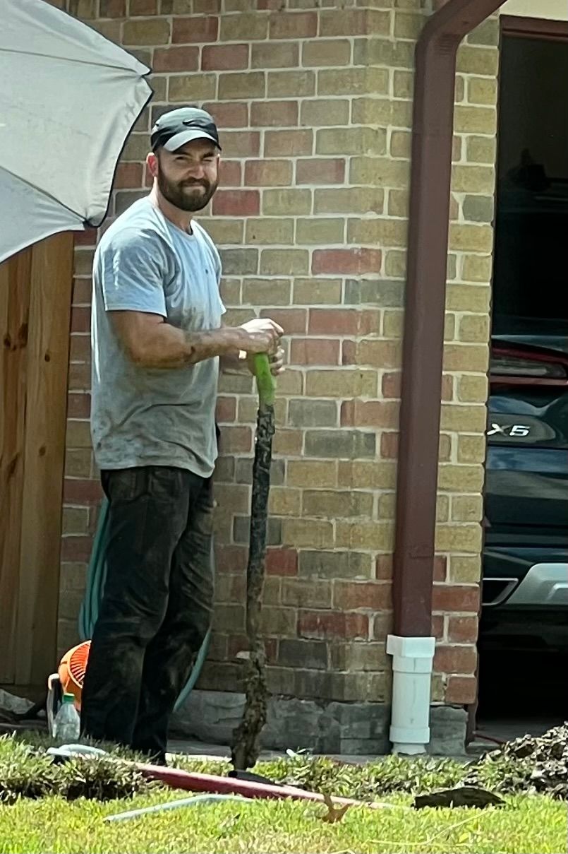 A man is standing in front of a brick building holding a hose.