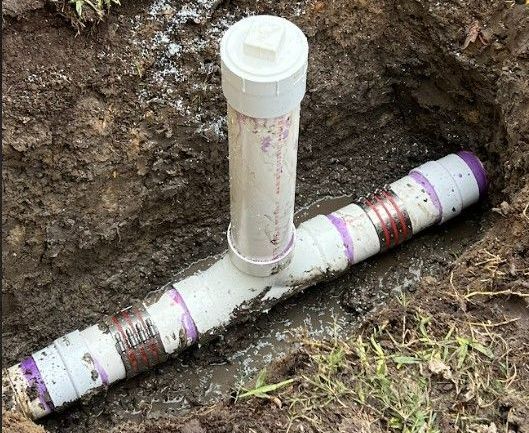 A pvc pipe is sitting in the dirt in a hole.