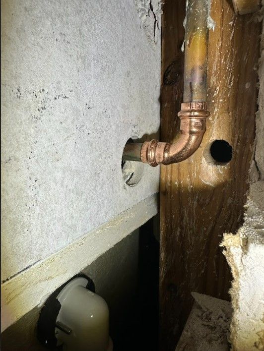 A copper pipe is coming out of a hole in a wall.