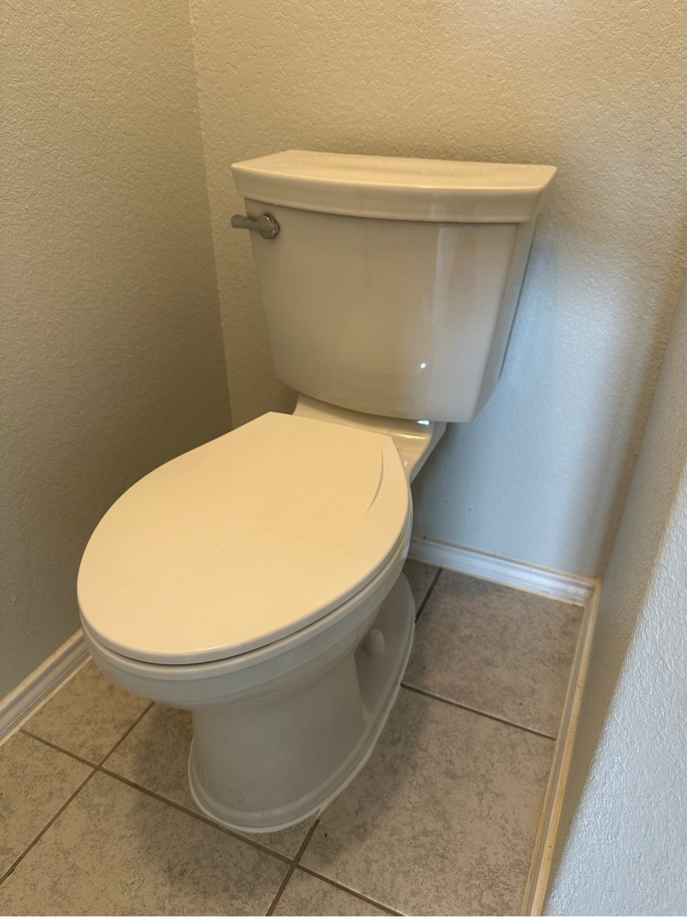 A white toilet is sitting on a tiled floor in a bathroom.