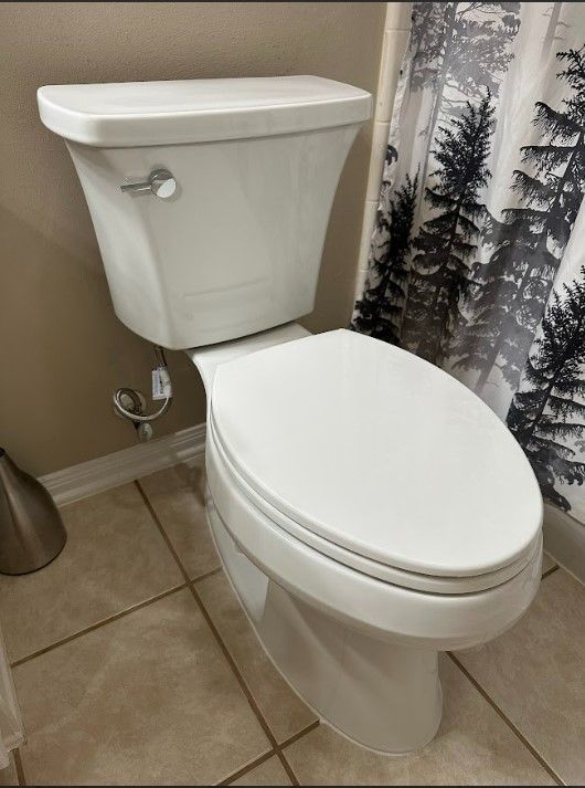 A white toilet in a bathroom next to a shower curtain with trees on it