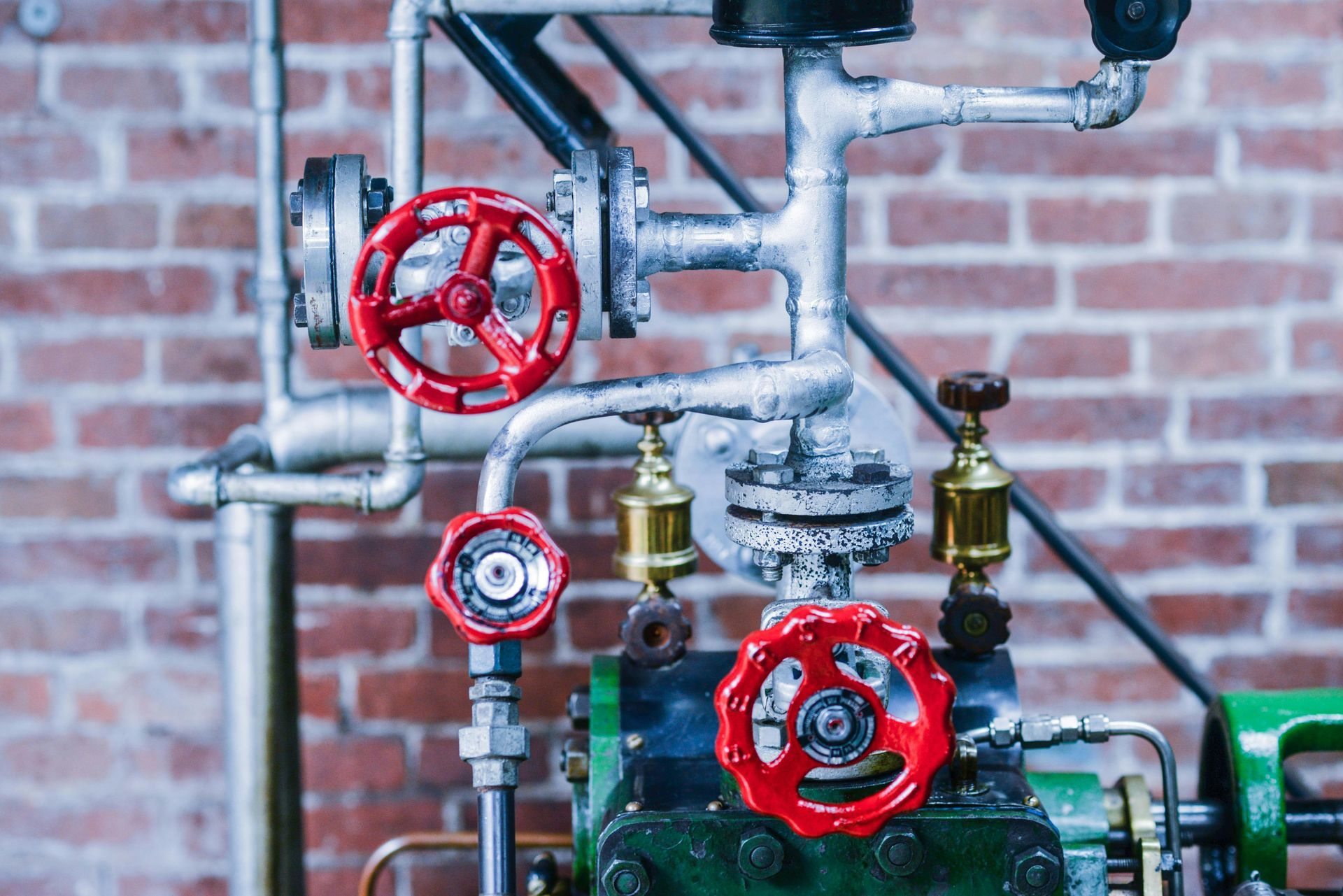 A close up of a machine with red valves and pipes in front of a brick wall.