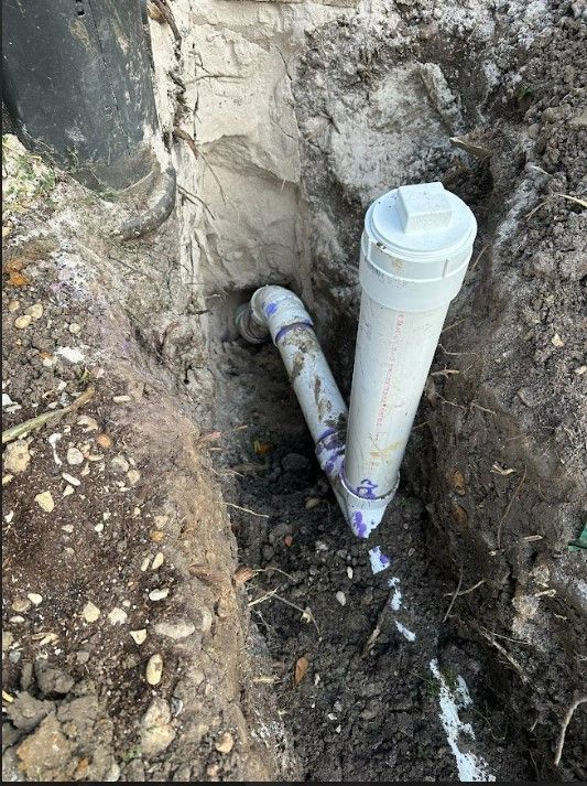 A white pipe is sitting in the dirt next to a wall.