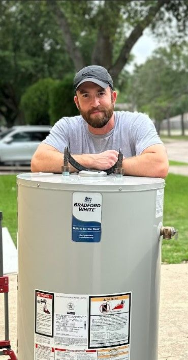 A man with a beard is leaning against a large water heater.