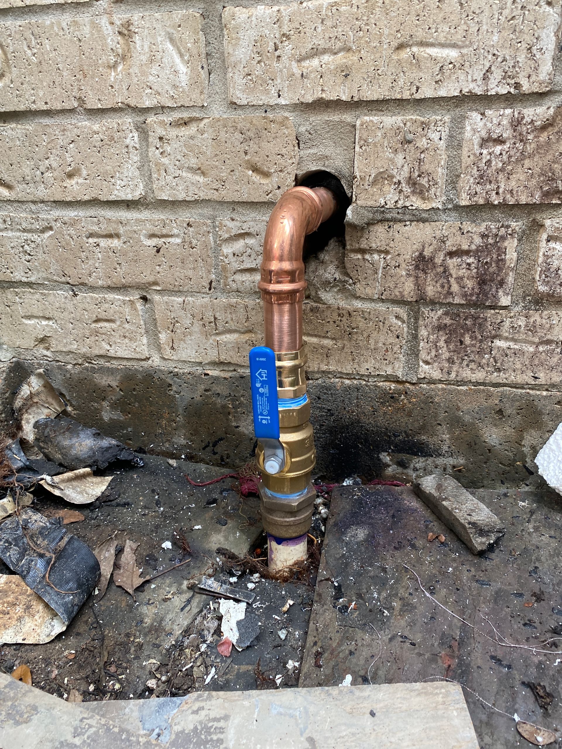 A copper pipe with a blue valve is attached to a brick wall.