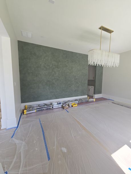 A room under construction with a large, textured, moss-green accent wall and a modern, tiered crystal chandelier above.