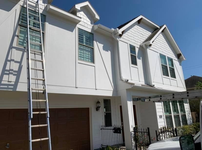 An extension ladder leans against the side of a two-story white suburban house with a brown garage door.