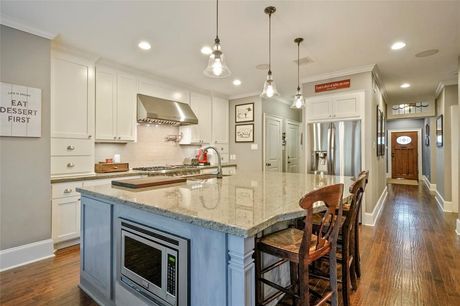 A bright kitchen featuring white cabinets, a large granite island with bar seating, and a microwave built into the base.