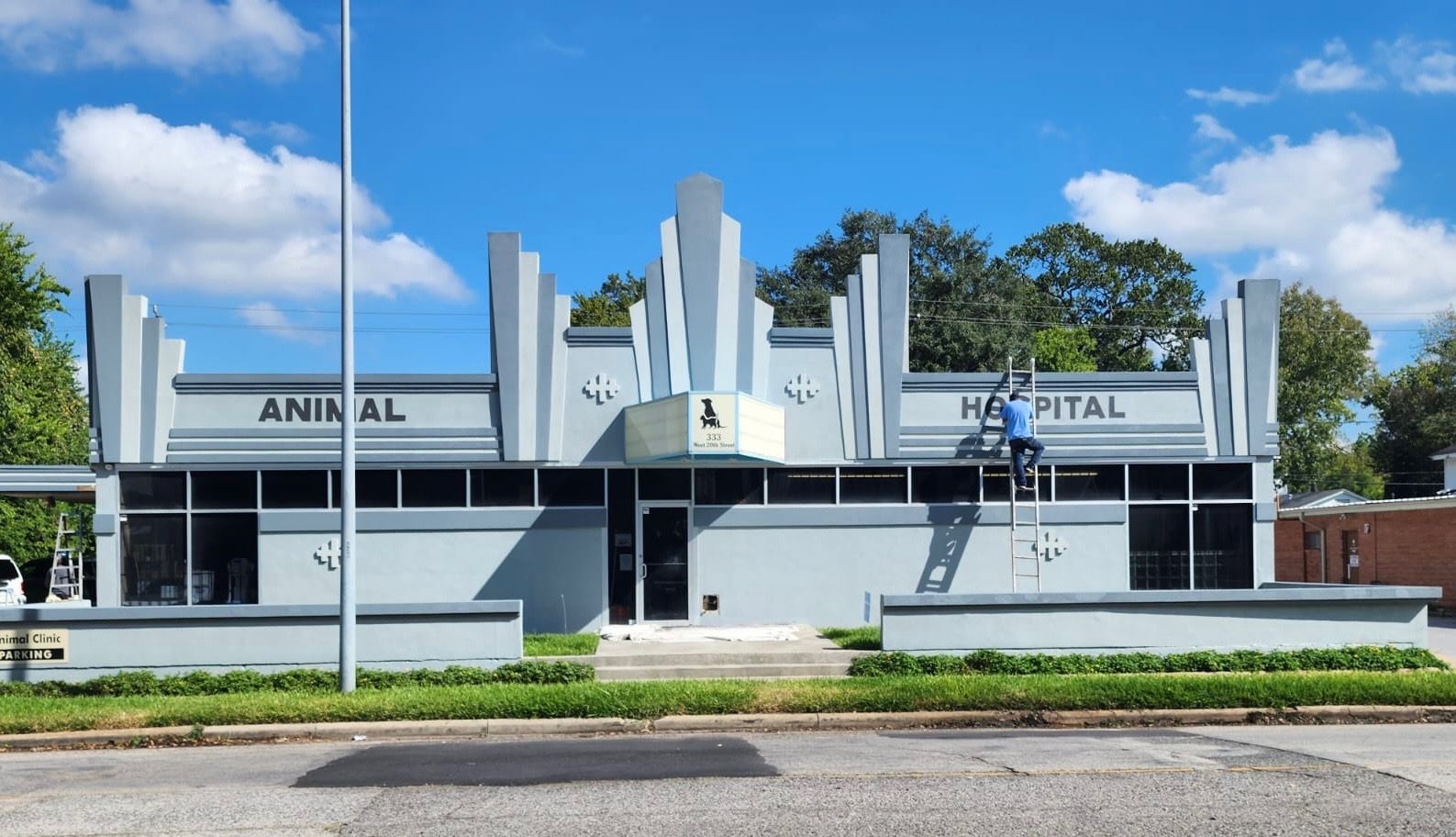 Art deco style animal hospital with gray exterior and a person on a ladder working on the building facade.