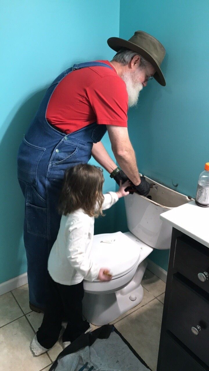 A man and a little girl are fixing a toilet in a bathroom.