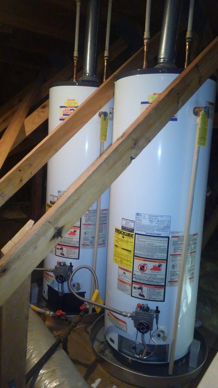 Two water heaters are sitting under a staircase in an attic.