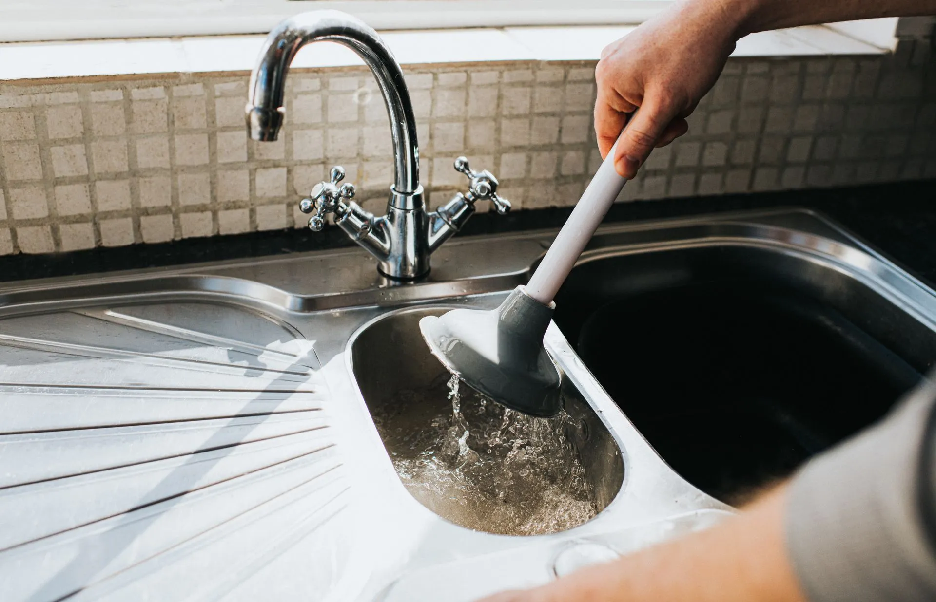 A person is using a plunger to clean a kitchen sink.