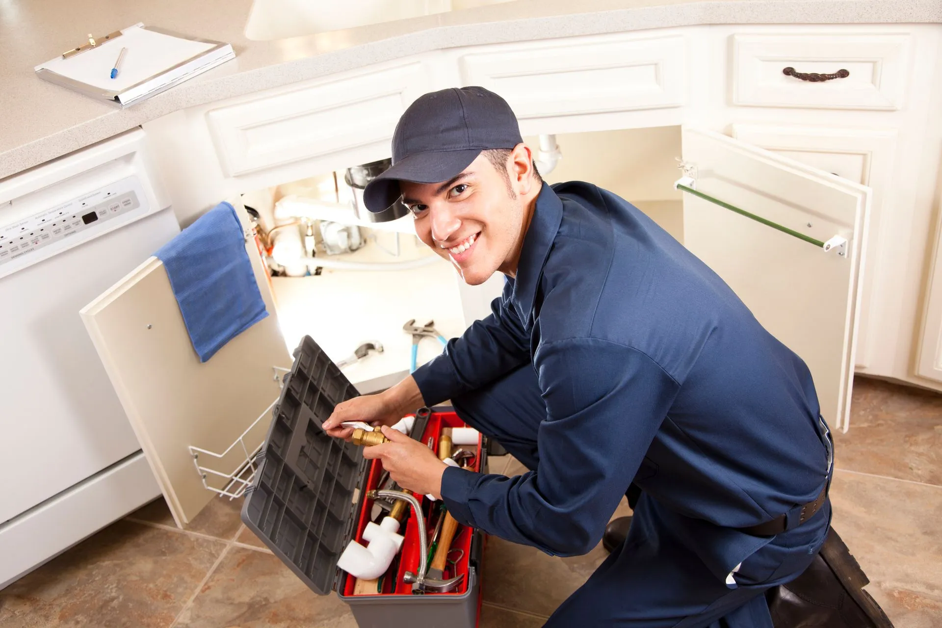 A plumber is working under a kitchen sink with a toolbox.