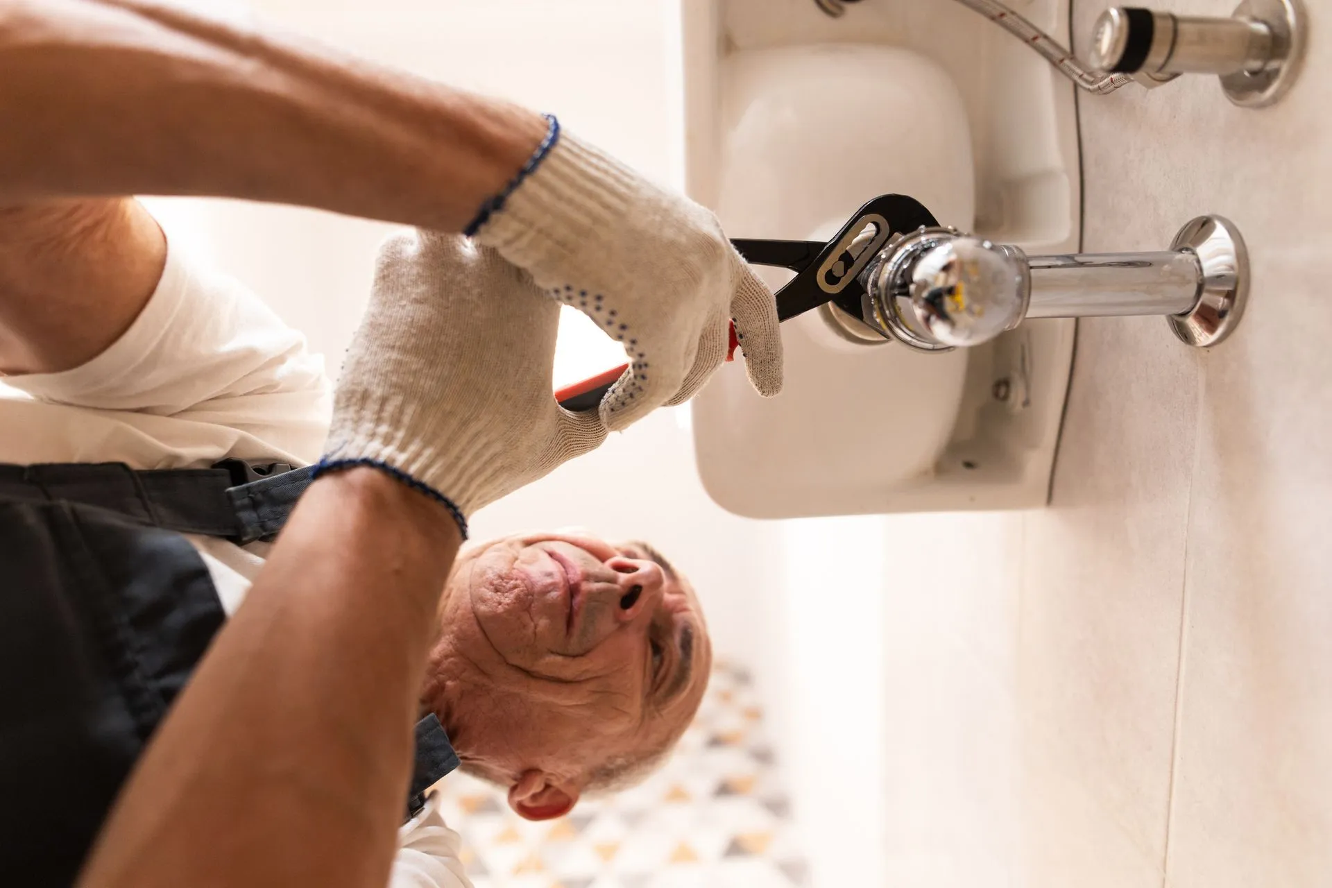 A man is fixing a sink with a wrench.