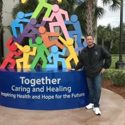 Man stands near a colorful sculpture of people; text reads, 