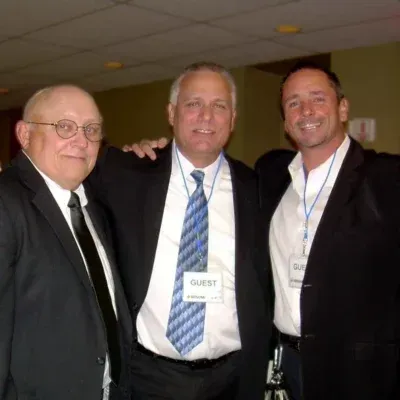 Three men in suits pose together, one with a 