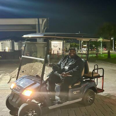 Man in dark uniform driving a golf cart at night.