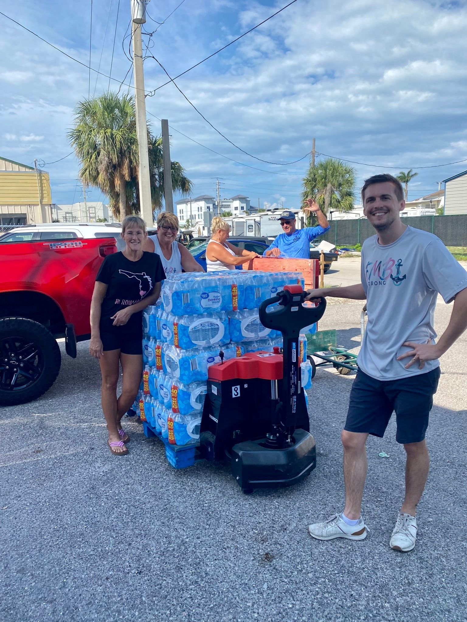 People stand with a pallet of water bottles by a red truck, aiding hurricane relief.