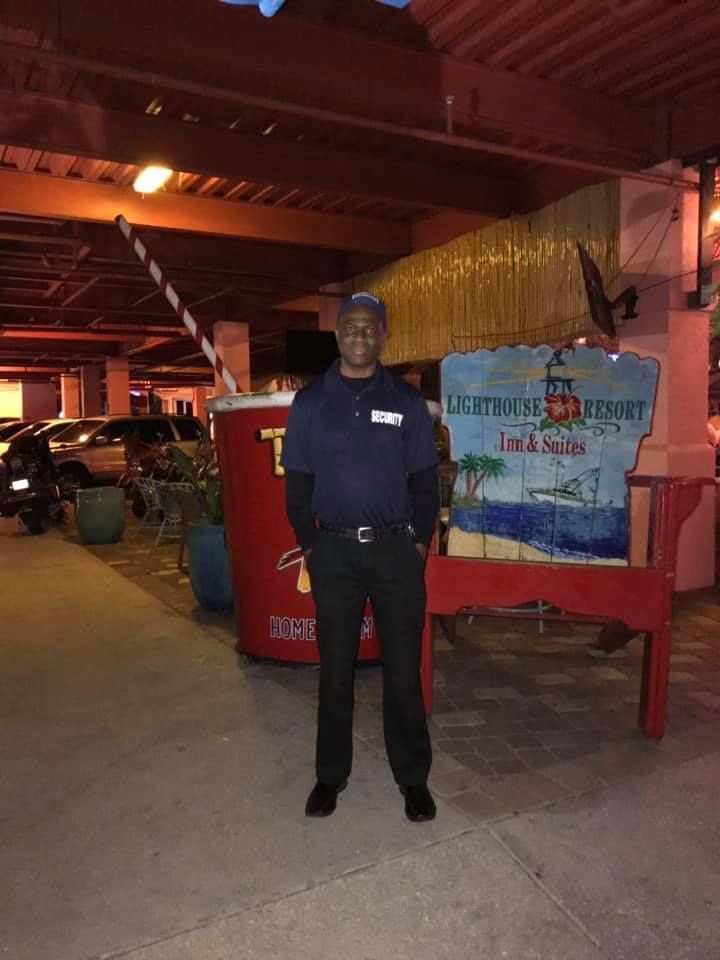 Man in uniform stands near a large drink sign and a painted sign in an outdoor setting.