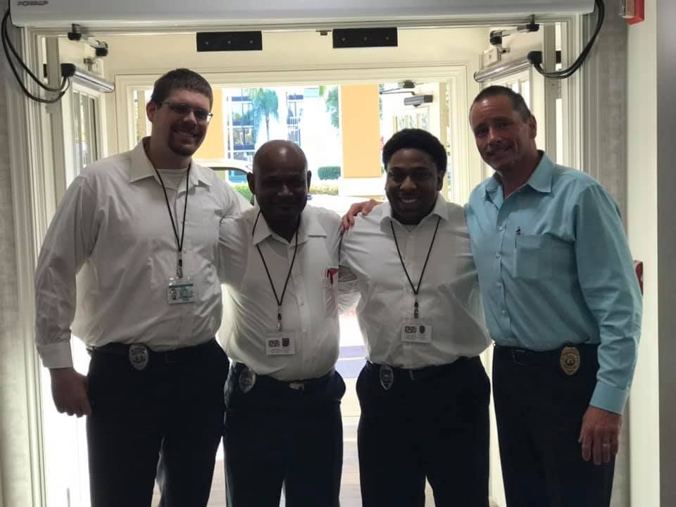 Four men in uniform pose near a doorway. They wear white shirts and black pants, smiling.