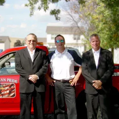 Three men pose in front of a red truck; two wear suits, the center one, a polo shirt, and sunglasses.
