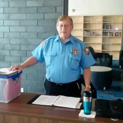 Security guard at desk, blue uniform, inside building, looking at the camera.