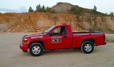 Red pickup truck parked on dirt in front of a tan rock face.
