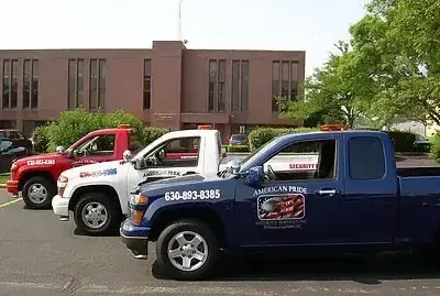 Three tow trucks of varying colors parked in front of a brick building, with an American flag emblem on the side.