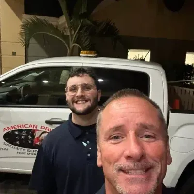 Two men smiling in front of a security truck with the company logo 
