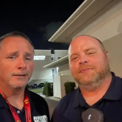 Two men, likely security, outside at night. One speaks while the other looks on.