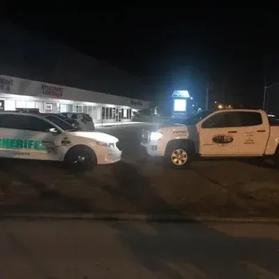 Sheriff's patrol car and service truck parked in front of a lit-up storefront at night.
