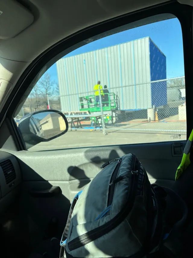 A person is sitting in a car looking out the window at a construction site.