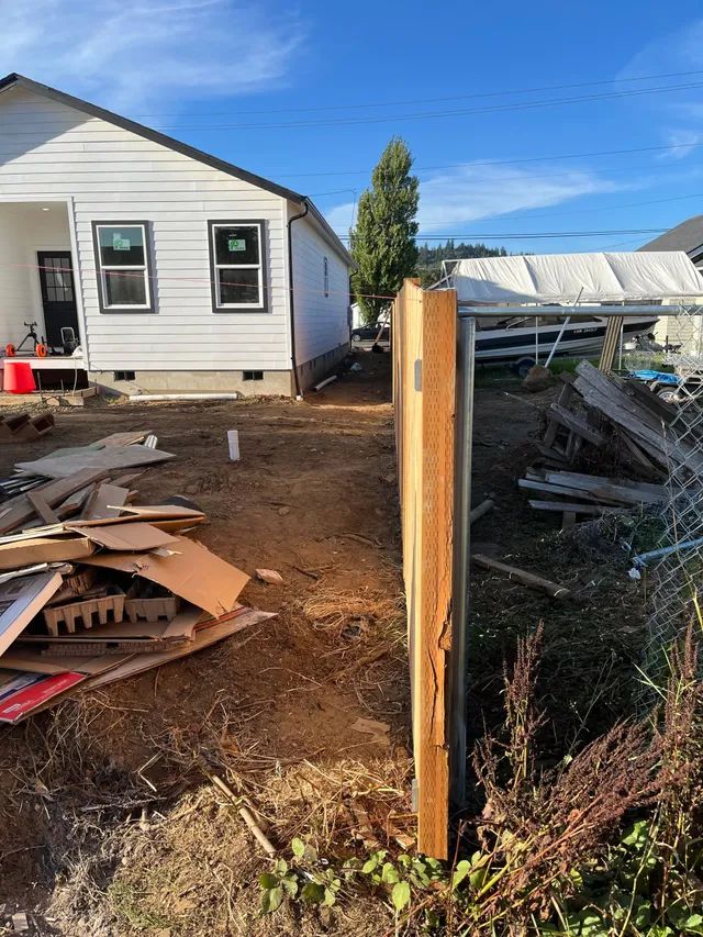 A wooden post is sitting in the dirt in front of a house.