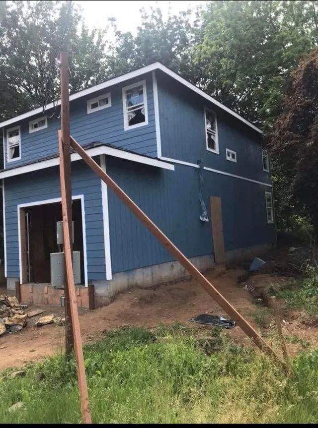 A blue house with white trim is surrounded by trees