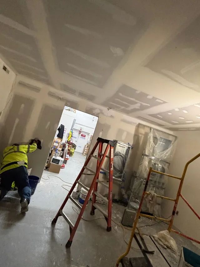 A man is working on a wall in a room with a ladder.