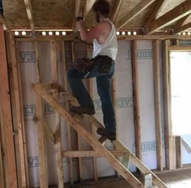 A man is standing on a wooden ladder in a house under construction