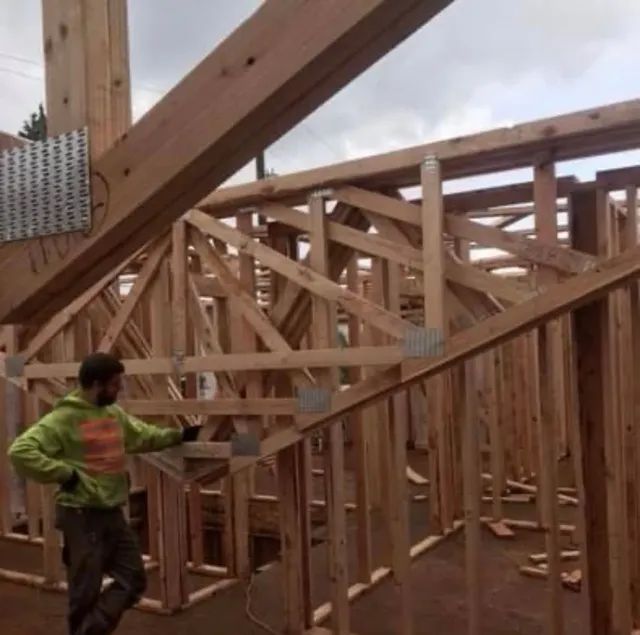 A man in a green hoodie is standing in a wooden structure
