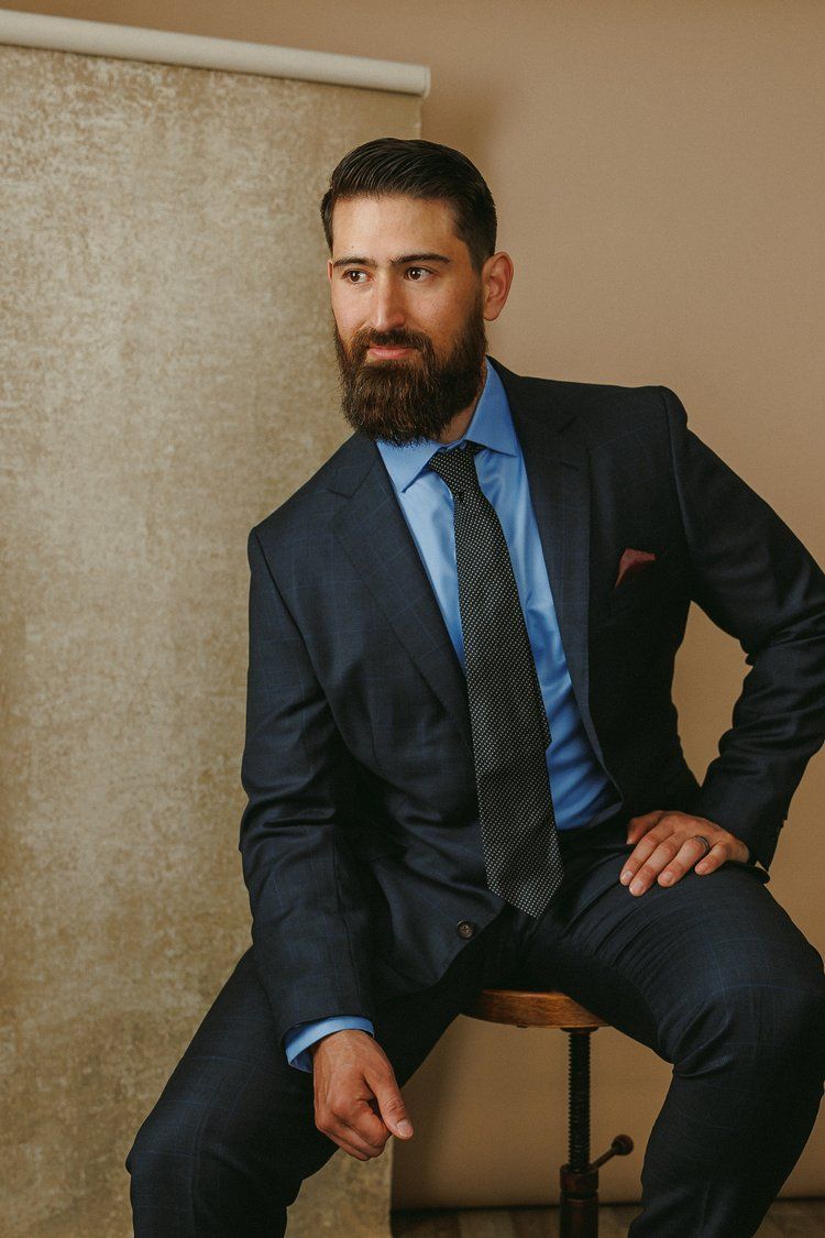 A man in a suit and tie is sitting on a stool.