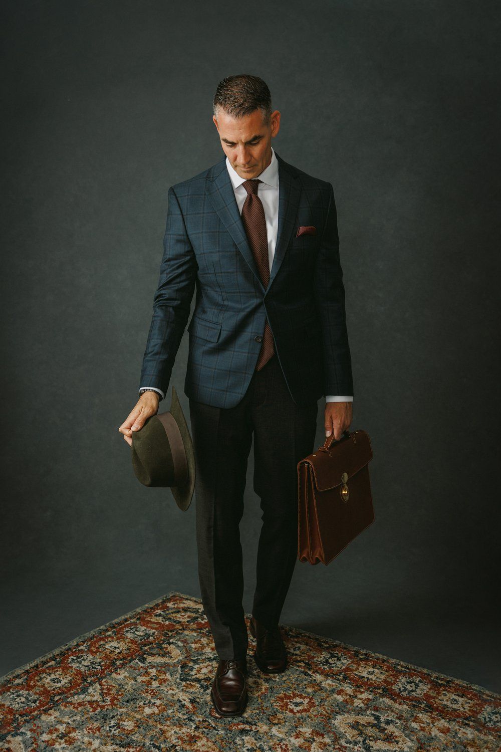 A man in a suit and tie is holding a hat and a briefcase.
