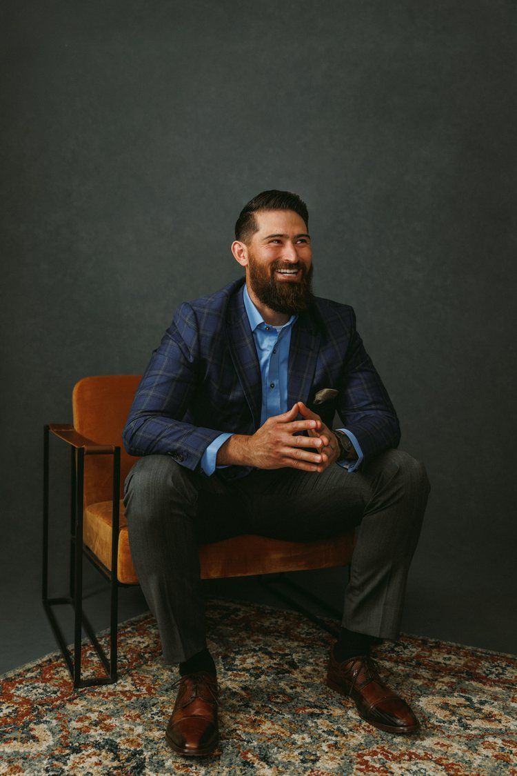 A man with a beard is sitting in a chair with his hands folded.